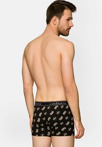 Czarne bokserki z wzorem kontrolera do gier w beżu, z markowym paskiem, widok z tyłu. Miękka tekstura tkaniny.