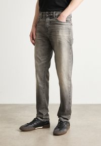 Jeans in denim grigio con un lavaggio sbiadito, design a cinque tasche e taglio dritto, abbinati a sneaker nere con dettagli marroni.