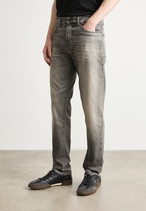 Jeans in denim grigio con un lavaggio sbiadito, design a cinque tasche e taglio dritto, abbinati a sneaker nere con dettagli marroni.