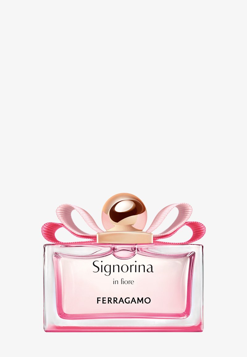 Flacon de parfum en verre rose clair rectangulaire avec un bouchon sphérique doré et un nœud en ruban rose, étiqueté "Signorina in fiore Ferragamo."