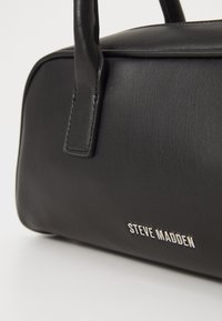 Czarna skórzana torebka z dwoma mocnymi uchwytami, gładką fakturą i srebrnym logo "STEVE MADDEN" z boku.