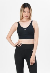 Black athletic bra with a round neckline and adjustable straps, featuring a small, silver logo at the center; smooth texture, fitted design.