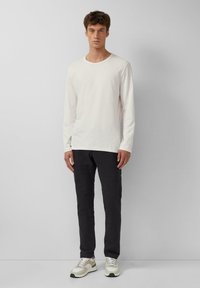 Crème lange mouwen overhemd, zwarte broek en multikleurige sneakers, met een eenvoudig ontwerp en een relaxte pasvorm. Geen duidelijke patronen zichtbaar.
