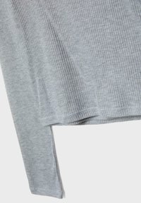 Tissu côtelé gris clair montrant la partie inférieure de la manche et l'ourlet d'un vêtement à manches longues avec un détail de texture verticale.