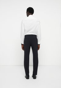 Kraljevsko modri hlače s krojem, ki se prilegajo telesu, z gladko teksturo, diskretnimi žepi na hrbtu in ravenim sprednjim delom; oblečene z belo srajco.