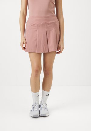 Gonna da tennis rosa pallido con pieghe, realizzata in tessuto morbido, vita aderente, abbinata a calzini sportivi bianchi e scarpe da ginnastica.