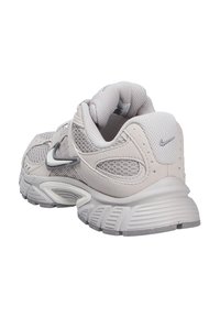 Zapatilla deportiva gris claro con paneles de malla y ante, suela gruesa y texturizada, y el logo reflectante de Nike en forma de swoosh en el lateral y el talón.