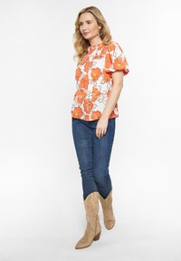 Blumige Bluse mit puffärmel in Orange und Weiß, kombiniert mit dunkelblauen Jeans und beigen Cowboy-Stiefeln mit dekorativer Stickerei.