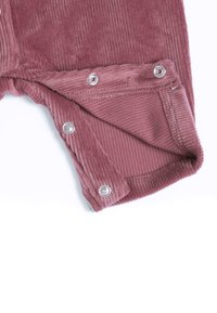 Gros plan d’un tissu en velours côtelé rose poussiéreux avec des boutons-pression argentés partiellement fixés sur un bord de vêtement plié.