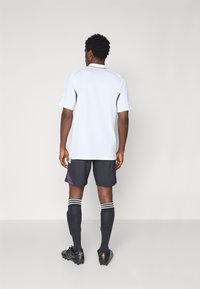 Hvid atletisk skjorte med sorte accenter, grå shorts med en lilla sidestykke, sorte knæhøje sokker og sorte støvler med guldfinish.
