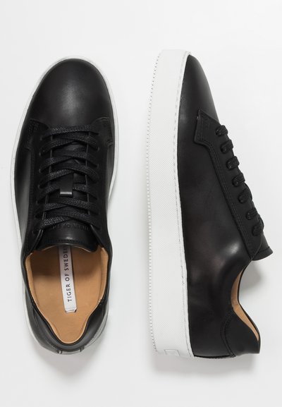 Sneakers in pelle nera con finitura liscia, dotati di una suola in gomma bianca, lacci texturizzati e una soletta beige con un logo sottile.