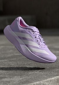 Gaiši violets skriešanas apavi ar baltām svītrām un akcentiem, ar elpojošu auduma augšdaļu un vieglu zoles dizainu.