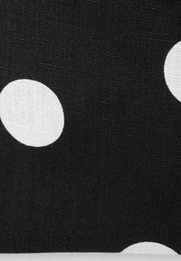 Tissu noir à gros pois blancs, montrant la texture détaillée du textile et le motif du tissage.