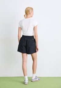 Black athletic shorts with an elastic waistband, two side pockets, and a subtle logo. Paired with a fitted white t-shirt and gray sneakers.