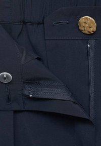 Navy kangas yenye kufungwa kwa kifungo, ikionyesha mfuko wa zipper ulifichwa na waistband ya elastic. Uso laini wenye maelezo ya kushona.