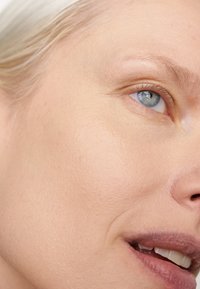 Närbild av en ljus hudton, som visar en jämn yta, små imperfektioner, blå ögon och naturliga läppar med minimal synlig smink.