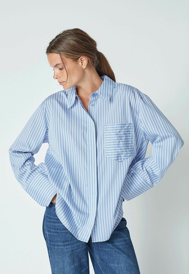 Blue and white striped button-up shirt with long sleeves and a chest pocket. Soft fabric with a relaxed fit and pointed collar.