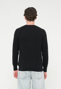 Μαύρο πλεκτό πουλόβερ με μακριά μανίκια, ριμπ λεπτομέρειες στους ώμους και ίσιο τελείωμα, συνδυασμένο με ανοιχτόχρωμο τζιν παντελόνι.