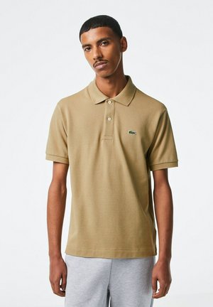 Beige polo skjorta i strukturerad textil med en knappslå med tre knappar, korta ärmar och en liten grön Lacoste-logotyp på bröstet.