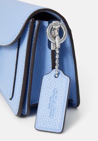 Coin d’un sac Coach en cuir texturé bleu clair avec anneau en métal argenté et étiquette en cuir assortie embossée de "Coach New York."