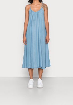 Lyseblå, ærmeløs kjole i midilengde lavet af blødt stof med en rynket halsudskæring og flydende silhuet, stylet med hvide sneakers.
