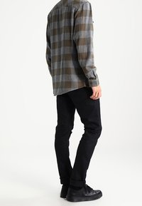 Grau- und braun kariertes Flanellhemd mit geradem Schnitt, kombiniert mit schwarzen Chinos und lässigen schwarzen Sneakers. Weiche Textur, Knopfmanschetten.