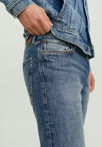 Jeans de mezclilla azul de corte ajustado, con cinco bolsillos, costuras en amarillo contrastante y un parche de cuero marrón en la cinturilla.