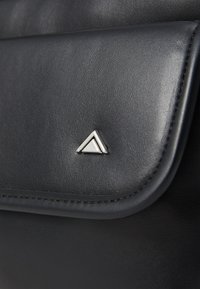 Borsa in pelle nera con texture liscia, chiusura a pattina e un accento triangolare in argento sul davanti.