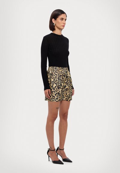 Top negro de manga larga acanalado combinado con shorts de estampado de leopardo amarillo. La modelo lleva puestas tacones negros de punta con correas en el tobillo.