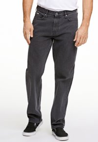 Vaqueros de mezclilla negros con un corte recto, diseño de cinco bolsillos y cremallera. Llevados con zapatillas negras y una camiseta blanca.