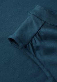 Tkanina w kolorze turkusowym o gładkiej teksturze posiada złożony rękaw oraz subtelne marszczenie, prezentując swobodny, dopasowany krój.