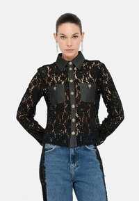 Camicia nera in pizzo con dettagli in denim, colletto classico, chiusura frontale con bottoni e due tasche sul petto. Design testurizzato con maniche lunghe.