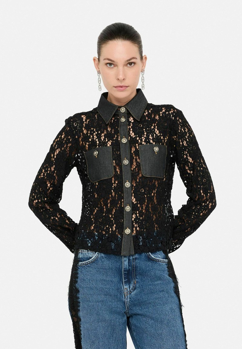Camicia nera in pizzo con dettagli in denim, colletto classico, chiusura frontale con bottoni e due tasche sul petto. Design testurizzato con maniche lunghe.