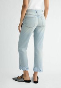 Jean en denim bleu clair avec une coupe cropped et des jambes larges. Présente une bordure en dentelle florale brodée à l'ourlet et aux poches arrière.