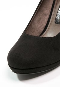 Chaussure à talon haut en suède noir avec un bout arrondi et une surface lisse. Présente un subtil détail de plateforme à l'avant et un talon élancé.