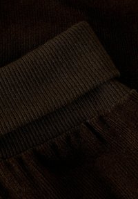 Ciemnobrązowy, prążkowany materiał z teksturowanym splotem. Posiada detal z podwiniętym mankietem i miękkie, gładkie wykończenie. Odpowiedni do codziennego użytku.