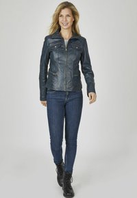 Blaue Lederjacke mit Reißverschluss, vier Taschen und einem Kragen; kombiniert mit dunklen Jeans und schwarzen Schnürstiefeln vor einem neutralen Hintergrund.