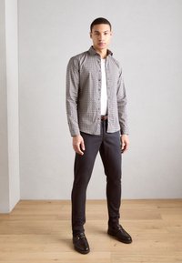 Košulja s gumbima i geometrijskim uzorkom, u sivoj i bijeloj boji, uparena s tamnim slim-fit hlačama i crnim mokasinkama. Glatke teksture i prilagođeni kroj.