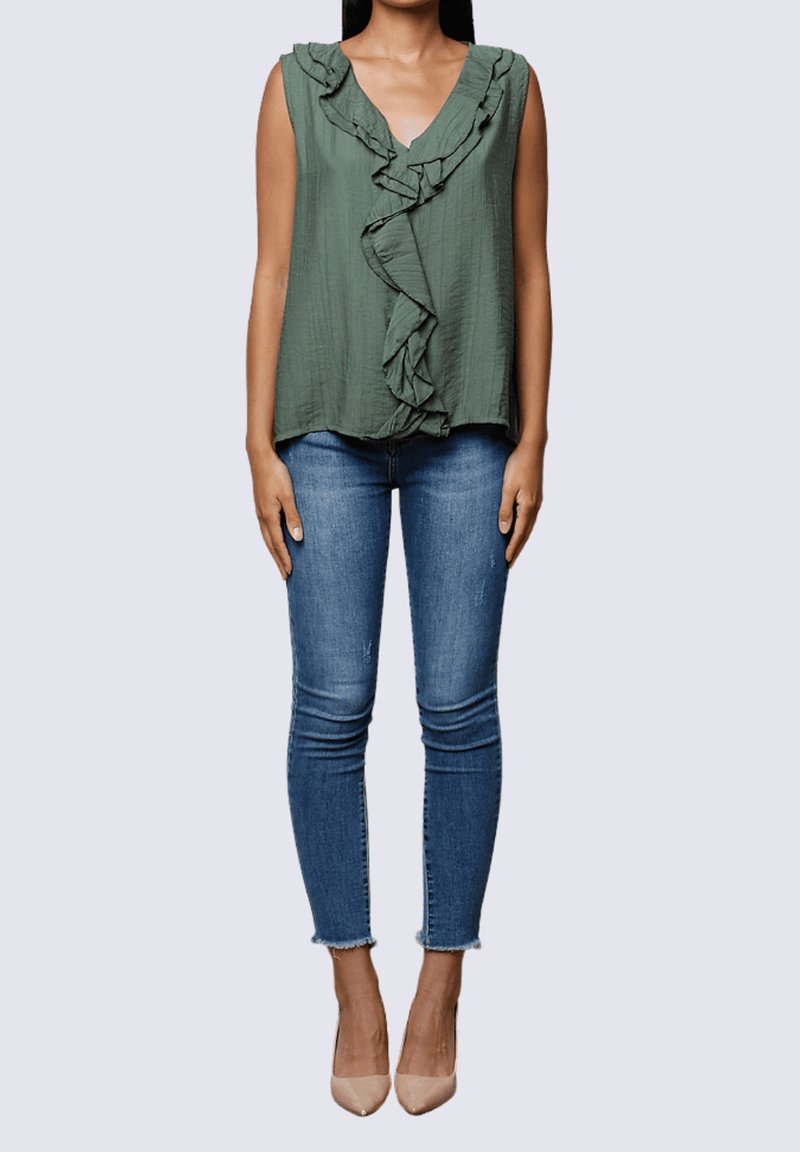 Top sin mangas de color verde oscuro con escote con volantes, combinado con jeans ajustados azules y tacones nude. Tela suave, diseño casual.