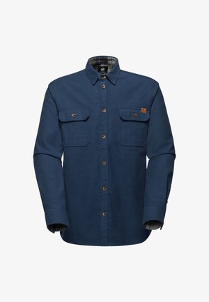 Camicia in flanella blu con due tasche sul petto, bottoni marroni e fodera a quadri visibile ai polsini. Presenta un colletto classico e un tessuto robusto.