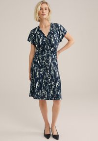 Robe bleu marine avec un décolleté en V, des manches courtes et une taille froncée. Présente un léger motif abstrait dans des tons de bleu et de blanc.