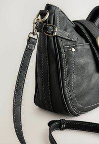 Sort læder skuldertaske med hvid syning, der har en flad bund, justerbar rem og guld metal hardware detaljer.