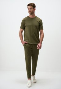 Olijf groene t-shirt met korte mouwen, gecombineerd met bijpassende slim-fit broek. De stof lijkt glad met een minimalistisch ontwerp. Witte sneakers maken de look af.