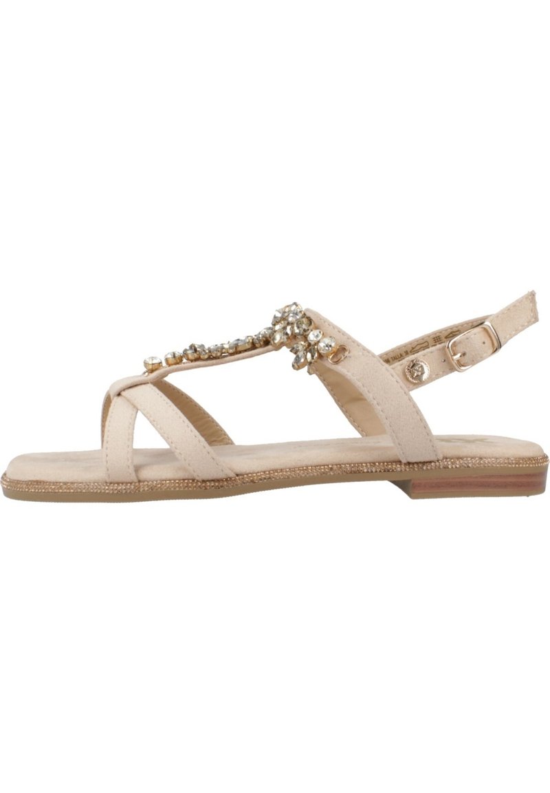 Sandalia beige con suela plana, con correas cruzadas, un acento joya y una correa trasera ajustable. Textura suave y diseño minimalista.