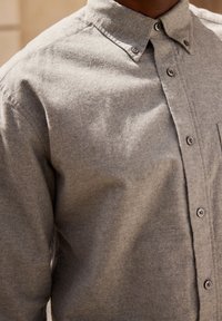 Grijze, button-up shirt van zachte stof, met een kraag, een voorzak en een afgeronde zoom. Zichtbare knopen en subtiele textuur.