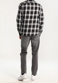 Zwart-witte geruite shirt met lange mouwen, grijze jeans en witte sneakers. Het shirt heeft een met knopen sluitende kraag en een ruitpatroon.