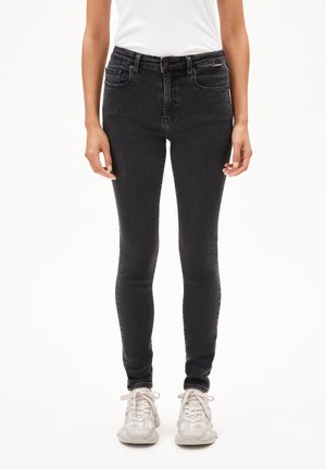 Strakke zwarte spijkerbroek van denim, met een hoge taille, steekzakken en een klassieke vijfzakkenontwerp. Gecombineerd met lichtgekleurde sneakers.