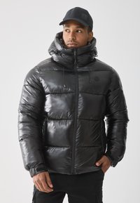Svart dunjakke med en blank, polstret design. Har høy krage, justerbare snorer og glidelås foran.