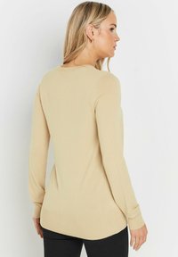 Pull beige à manches longues avec un col rond, des poignets et un ourlet côtelés. Texture douce avec une finition lisse, conçu pour un ajustement décontracté.