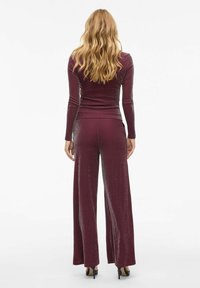 Haut bourgogne à manches longues et pantalon à jambes larges en tissu scintillant. Présente une silhouette ajustée et une texture subtile.